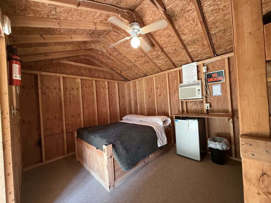 Double bed, ceiling fan, mini fridge and air conditioner inside a rustic cabin