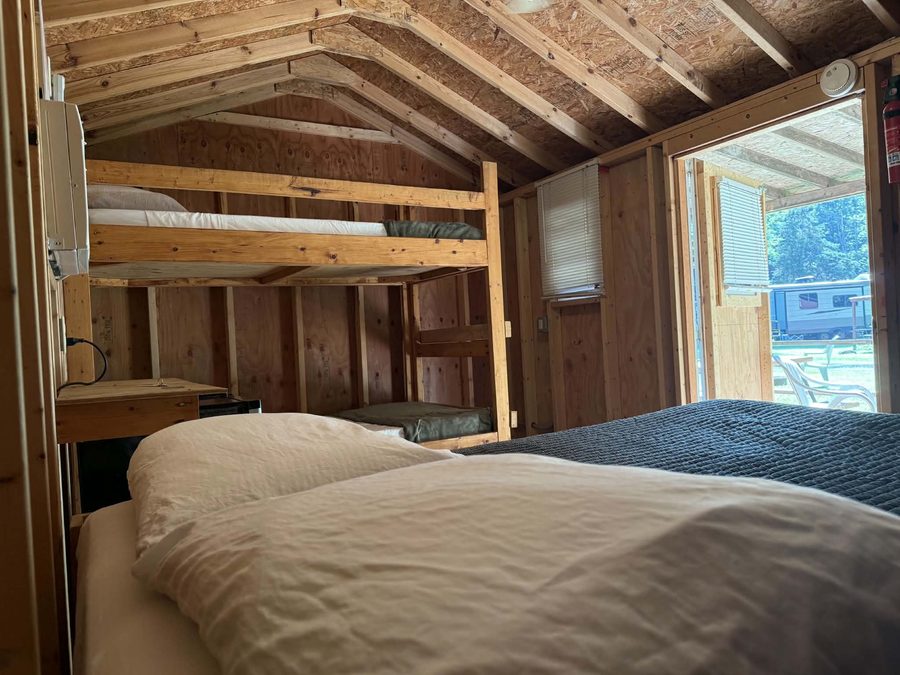 Bunk beds and double bed inside a rustic cabin, with the door open to the covered porch